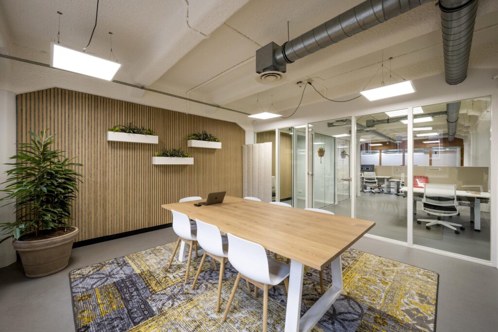 Modern meeting room on Van Diemenstraat with a wooden table, white chairs, and decorative wall-mounted plants.